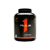 A black plastic container of Rule 1 R1 Whey Protein Isolate with a label that features the brand logo and product name, against a white background.